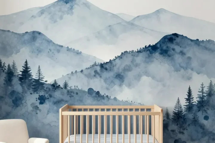 A modern nursery with a blue watercolor mountain mural behind a light wood crib.