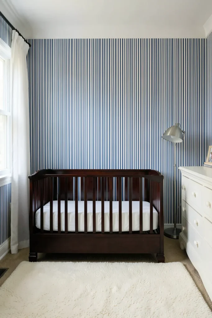 A traditional nursery with thin blue and white ticking stripe wallpaper and a dark wood crib.