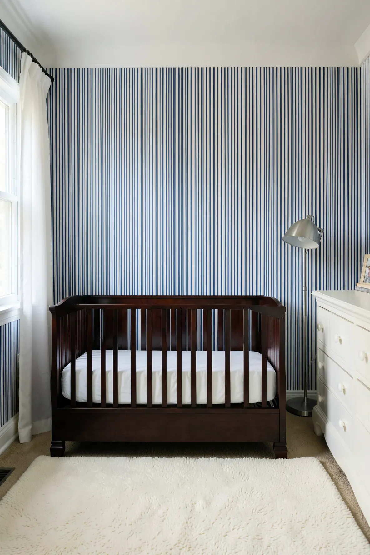 A traditional nursery with thin blue and white ticking stripe wallpaper and a dark wood crib.