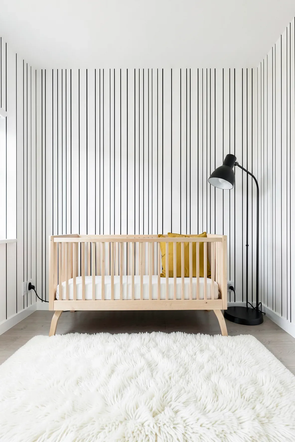Modern nursery with thin black pinstripe wallpaper and a plush white rug.
