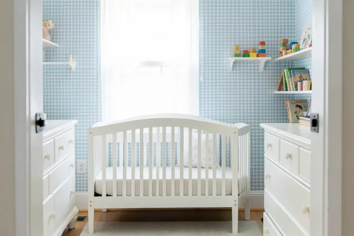 A traditional boy's nursery with light blue gingham wallpaper, a white crib, and light wood floors.
