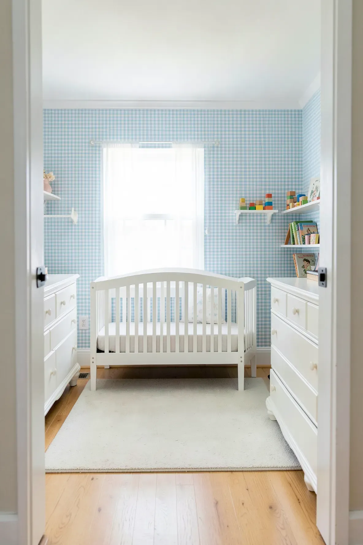 A traditional boy's nursery with light blue gingham wallpaper, a white crib, and light wood floors.