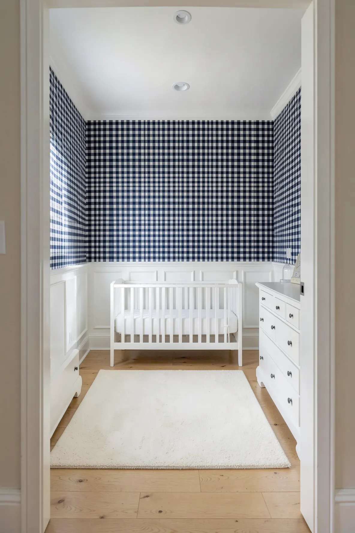 A traditional nursery with navy blue gingham wallpaper, white wainscoting, and white furniture.