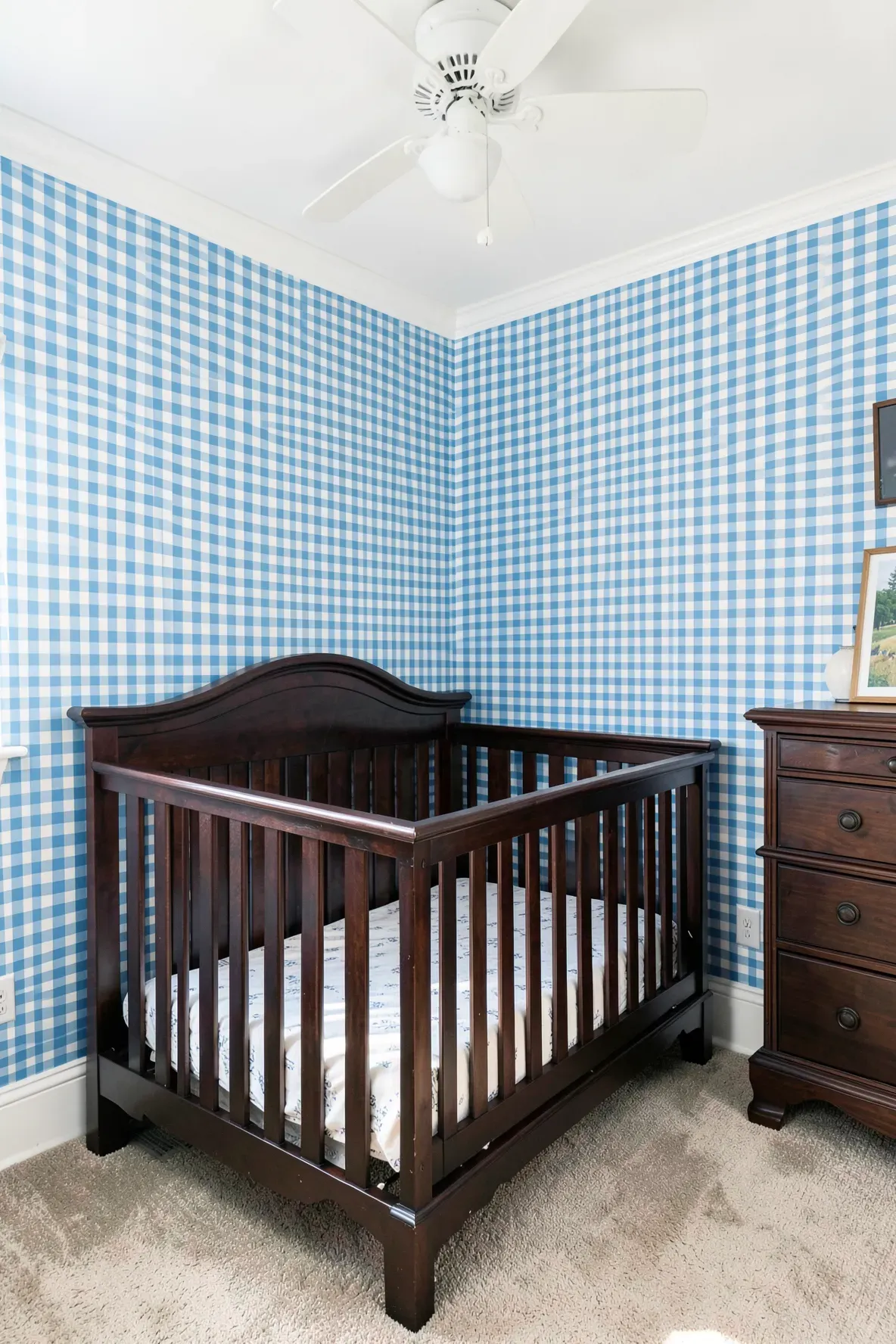 Sky blue gingham wallpaper in a nursery with a dark espresso wood crib and bright lighting.