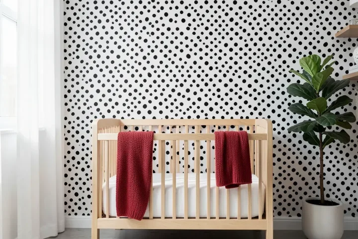 A modern nursery with black and white Dalmatian spot wallpaper behind a light wood crib.