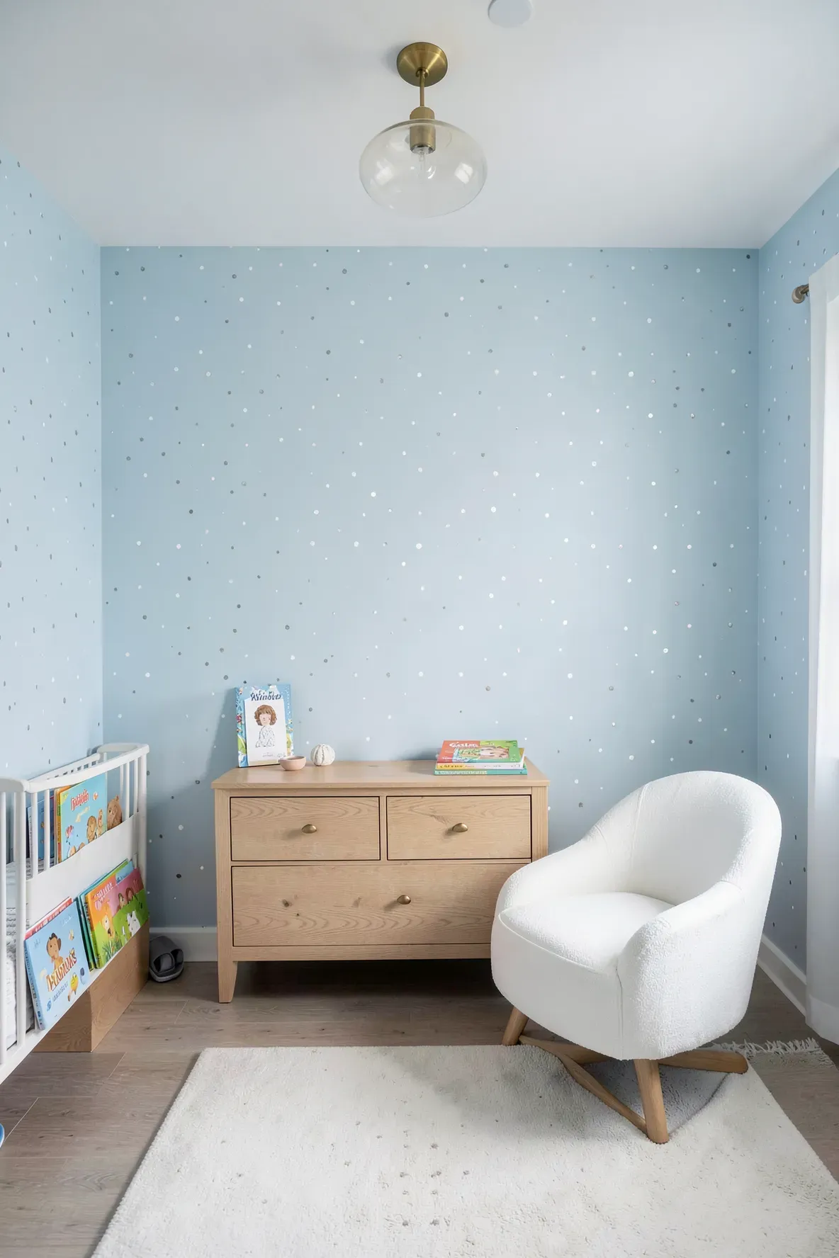A serene nursery with pale blue and silver dot wallpaper and light oak furniture.