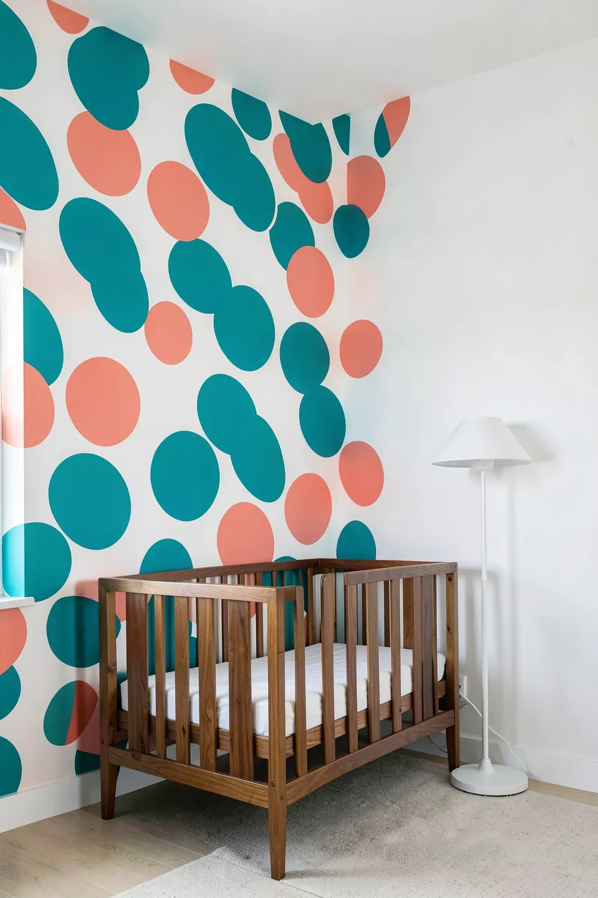 A bold nursery accent wall with large teal and coral polka dots next to a white wall.