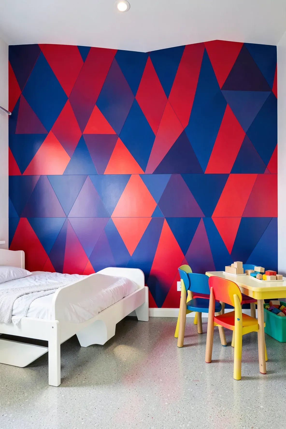 A toddler room featuring a bold red and blue interlocking triangle geometric accent wall.