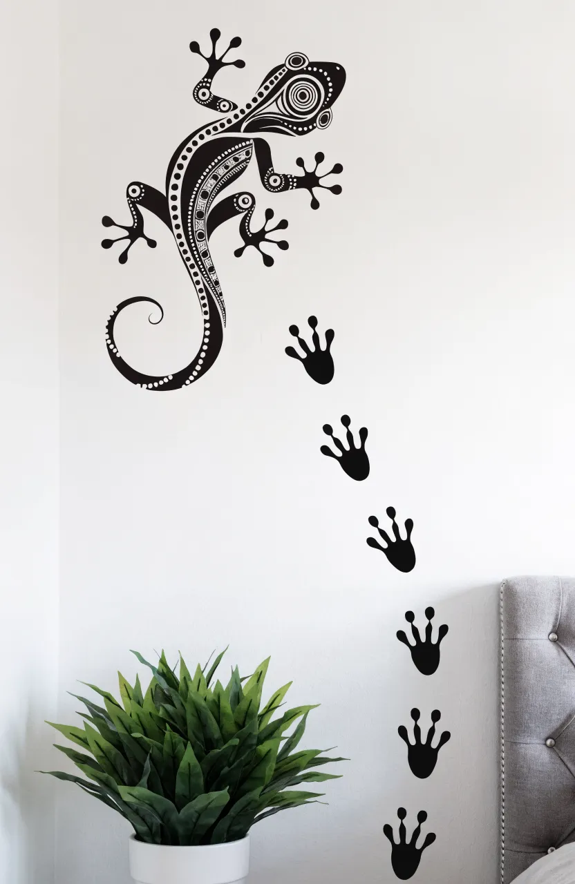 Black vinyl gecko decal with tribal patterns and a trail of footprints on a flat white matte wall.