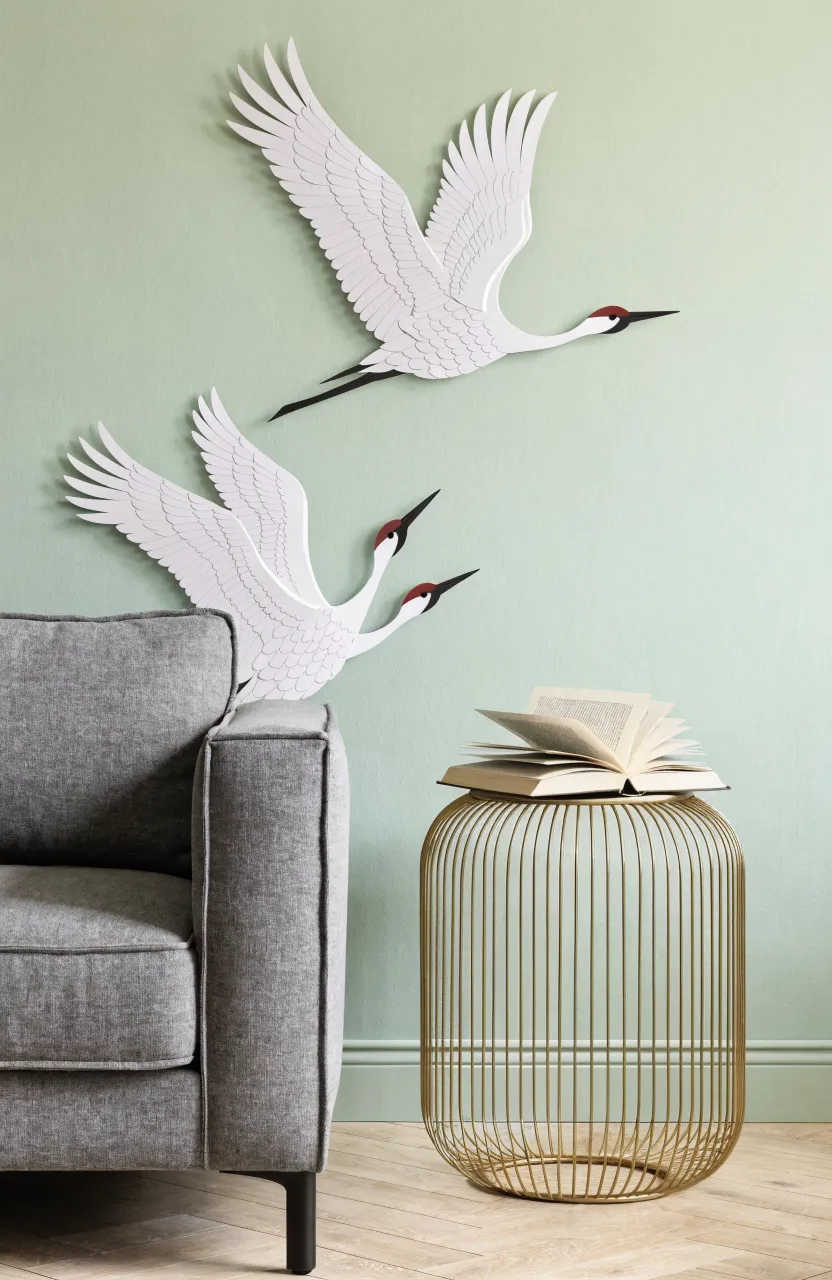 Minimalist living room with soft sage walls and white flying crane decals above a gray sofa.