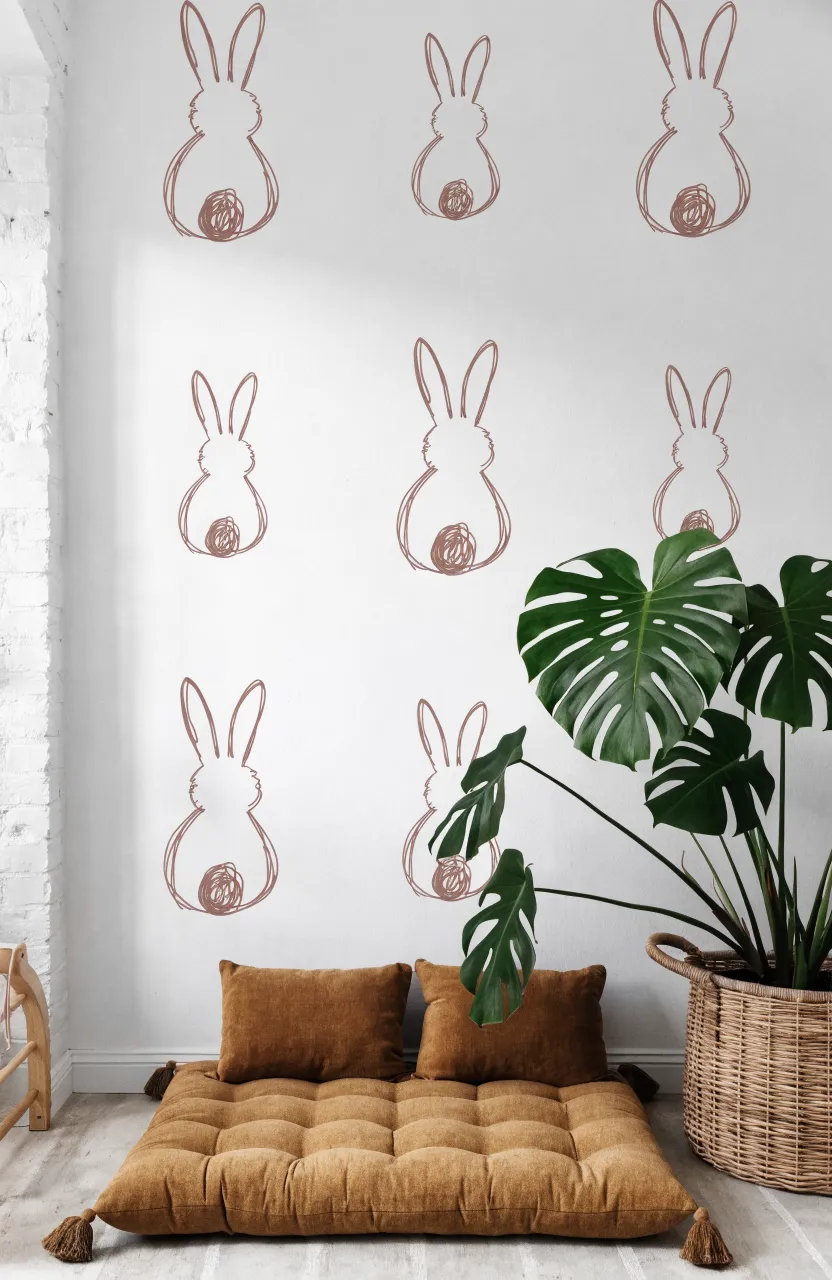 White wall with repeating mauve bunny silhouettes from behind showing ears and fluffy tails next to a floor cushion.