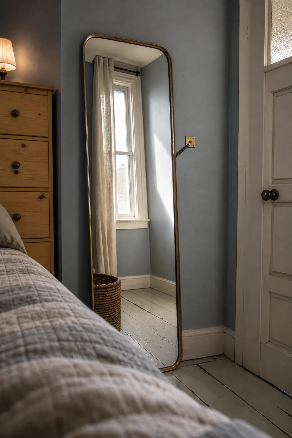 Narrow full-length mirror reflecting daylight in a tiny bedroom