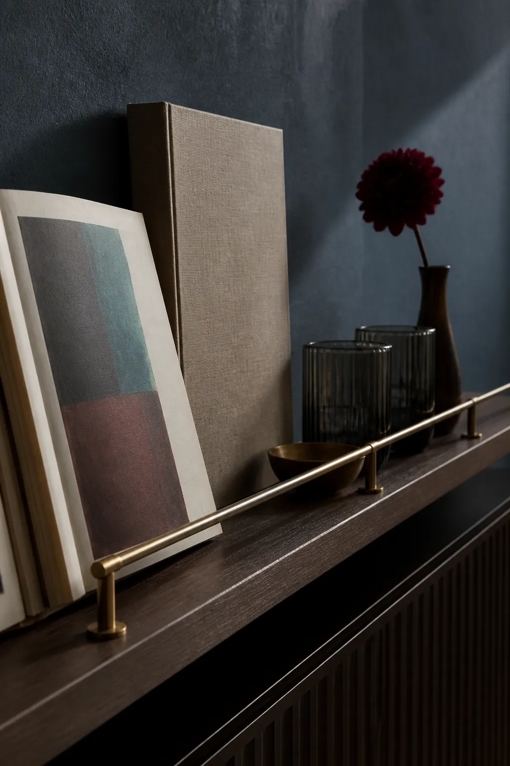 Moody walnut ledge layered with stacked books and dark framed artwork