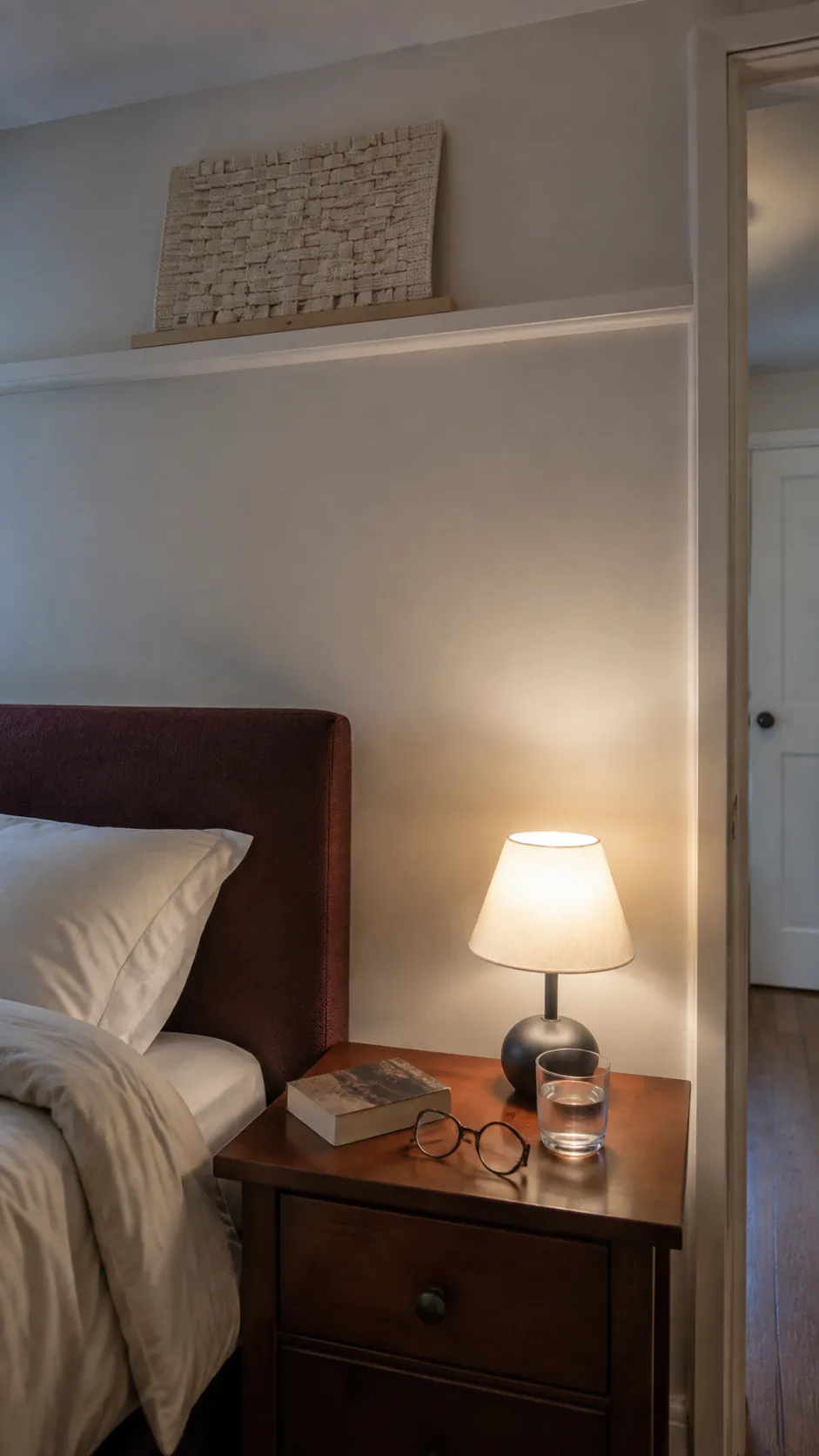 Bedside storage and a quiet woven display above a bed at dusk