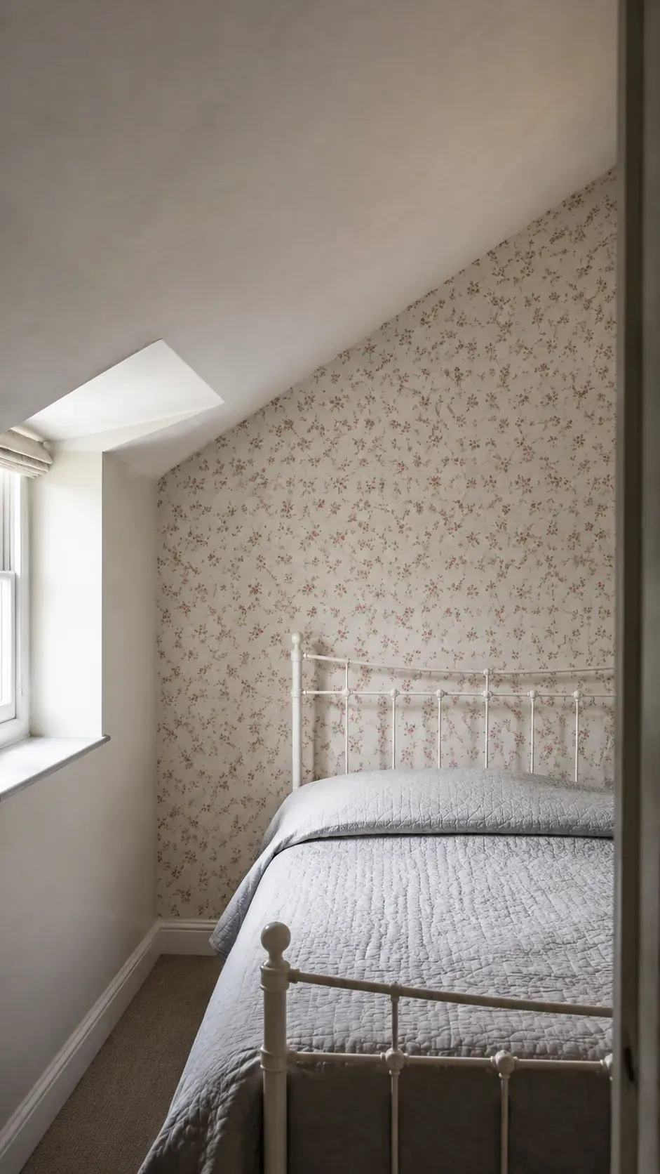 Small floral wallpaper on a vertical attic wall behind an iron bed