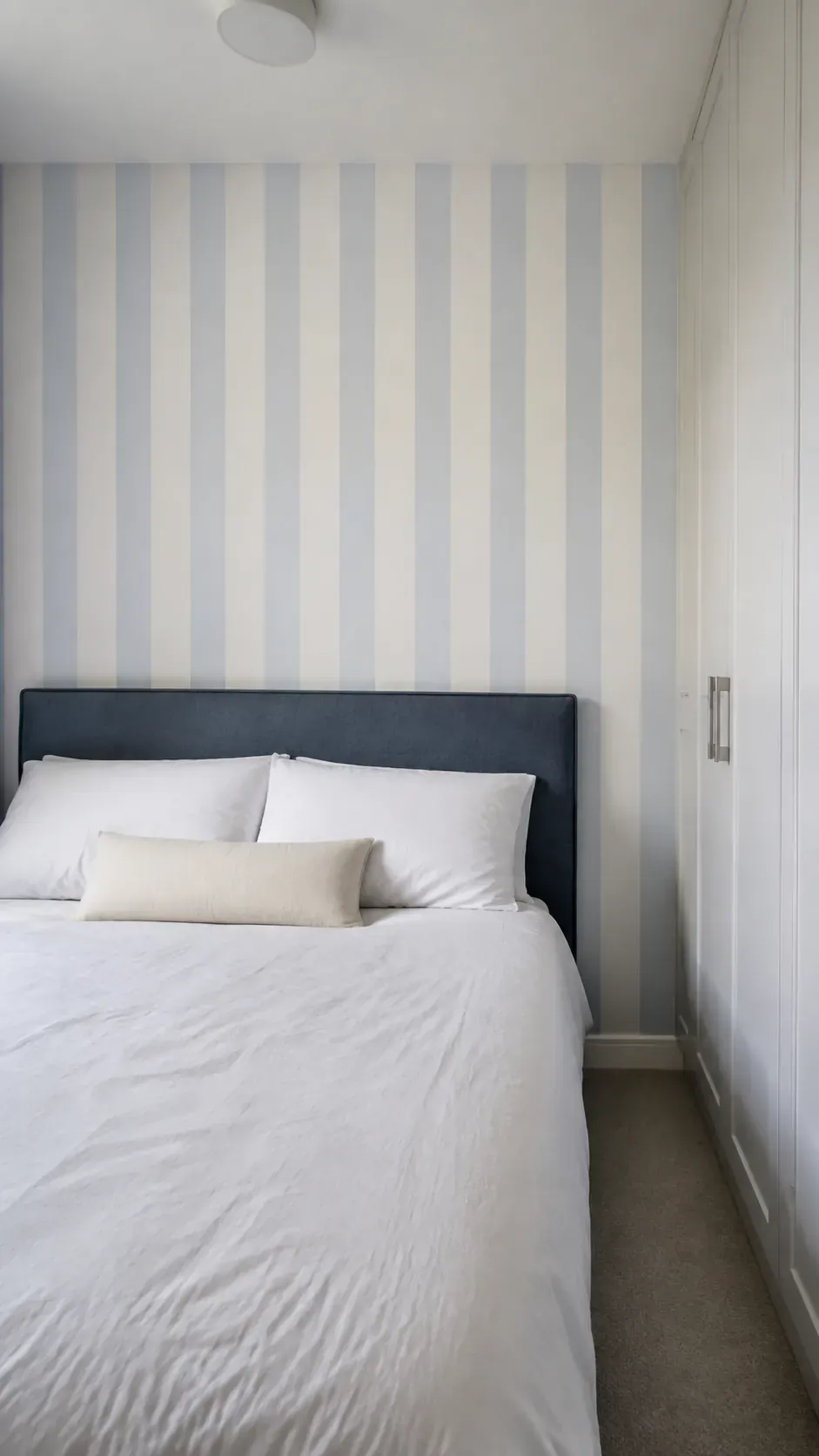 Soft vertical striped wallpaper behind a low blue upholstered headboard