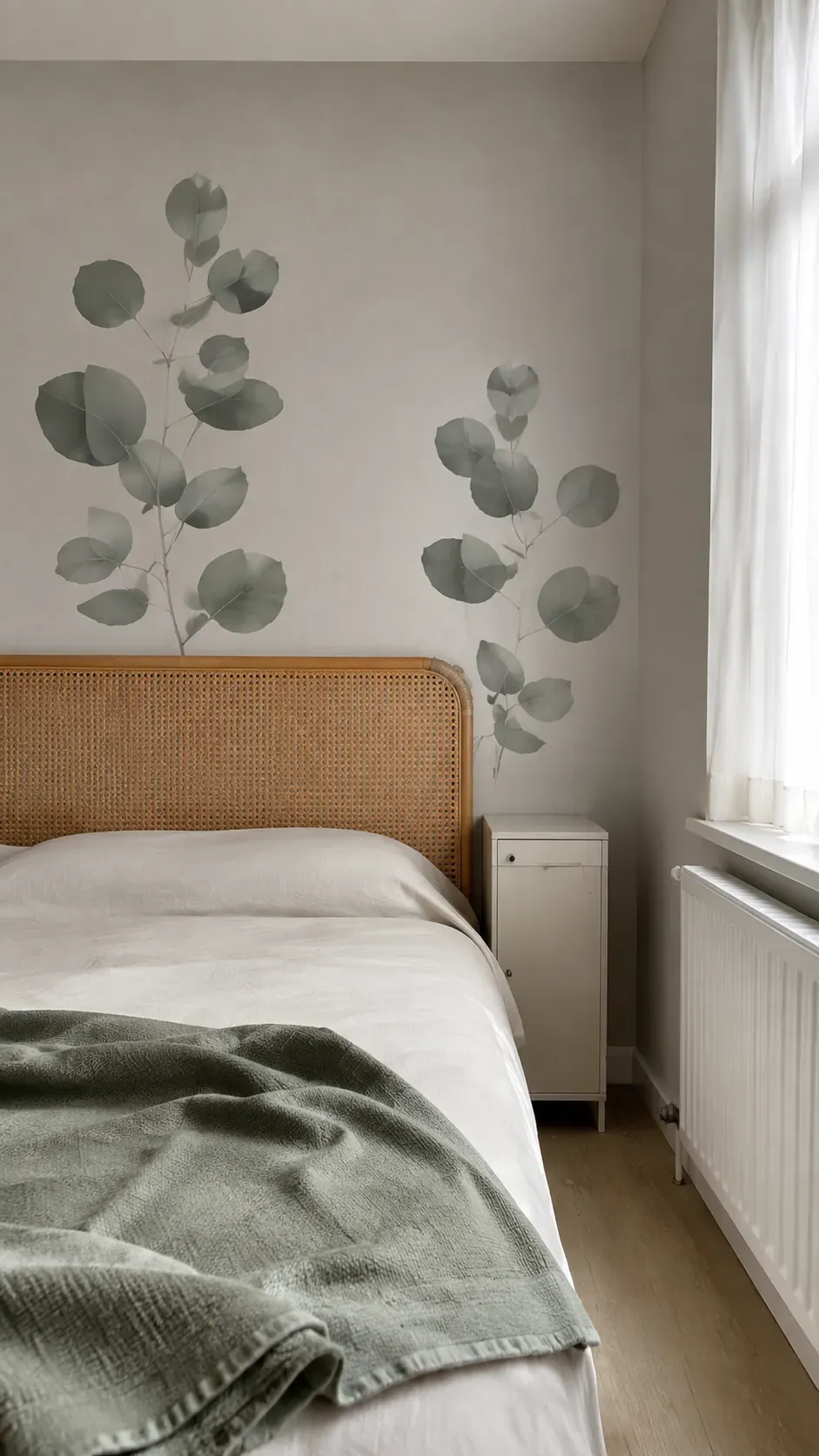 Large sage leaf wallpaper above a cane headboard in an apartment