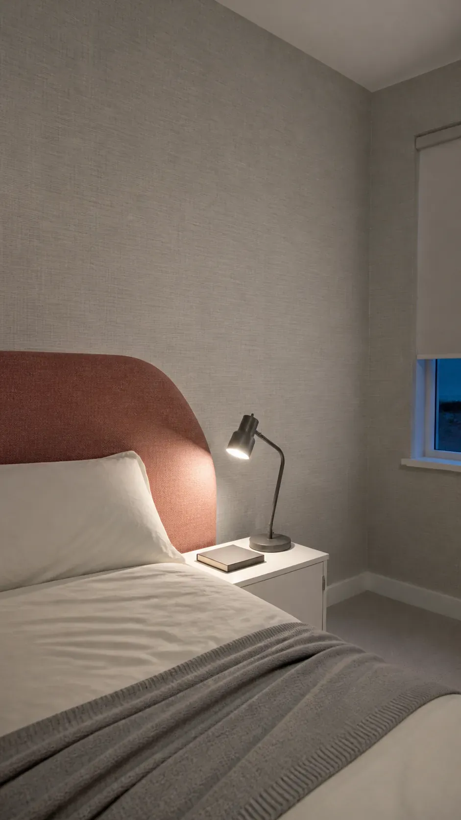Quiet linen effect wallpaper behind a shaped rust upholstered headboard