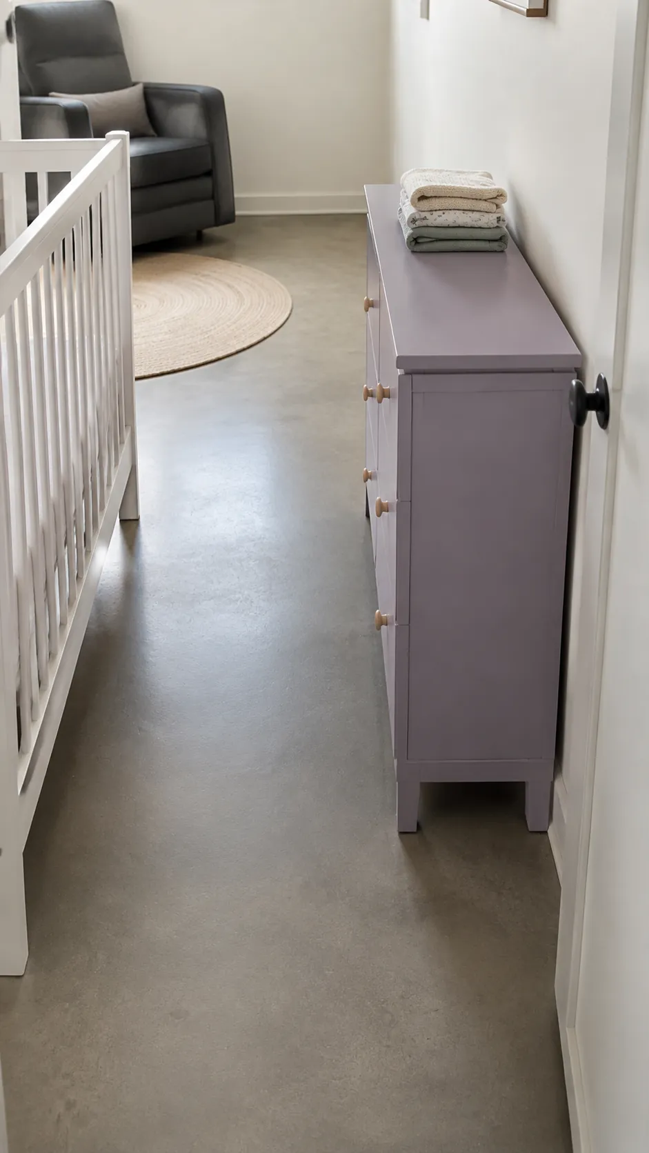 Capture the practical benefit of a shallow dresser at a nursery pinch point, with its modest depth visibly preserving a passage opposite the crib