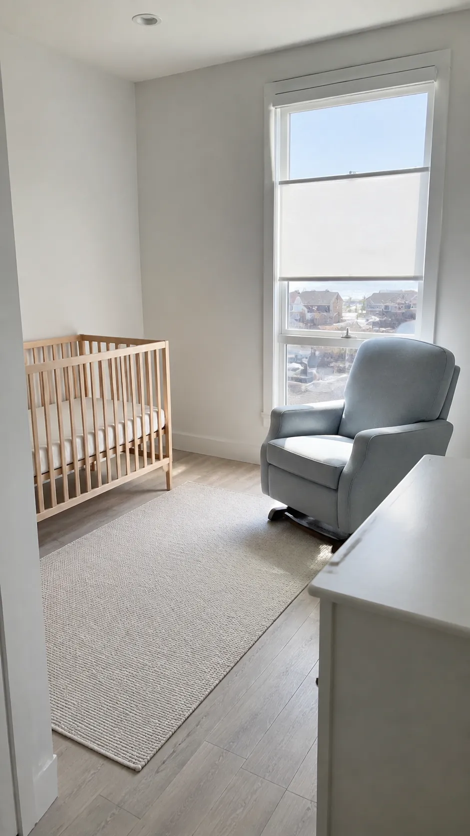Present a bright window side as a sensible sitting area while the crib occupies a separate solid interior wall