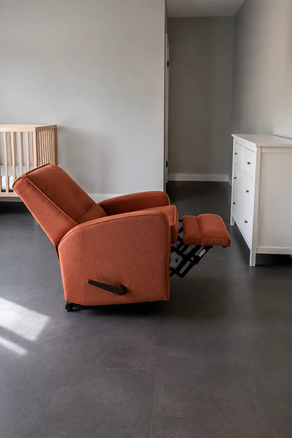 Demonstrate the full operating space of a nursery recliner glider by photographing it extended with clear floor around the footrest and back