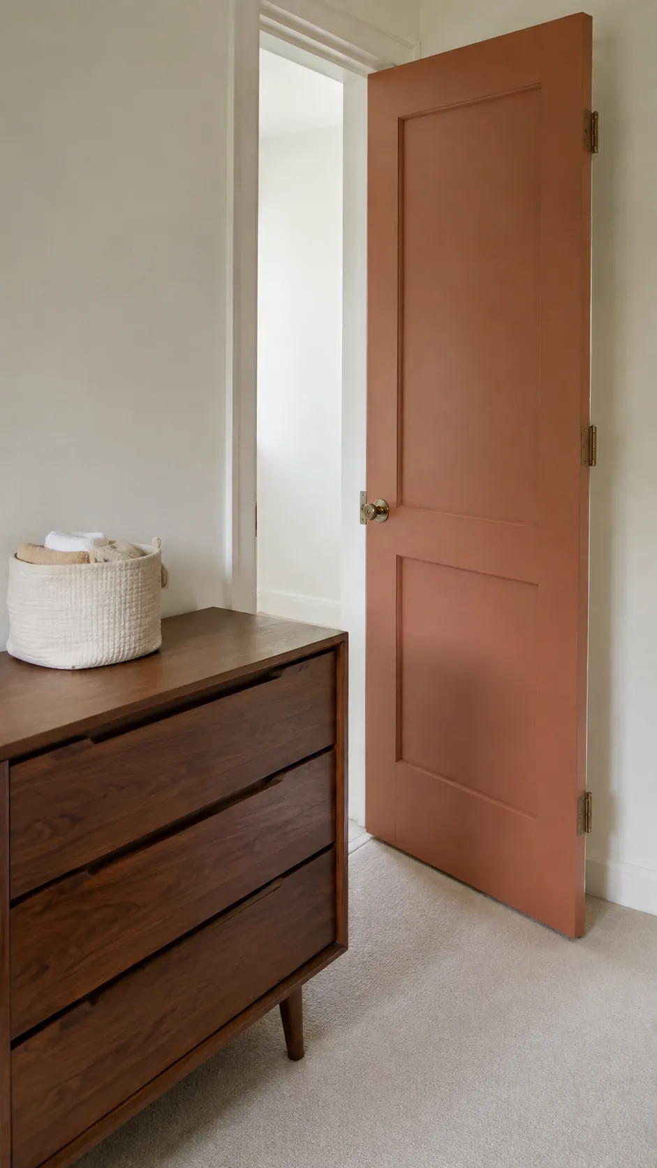 Cream and Walnut nursery with walnut dresser next to a muted terracotta painted door