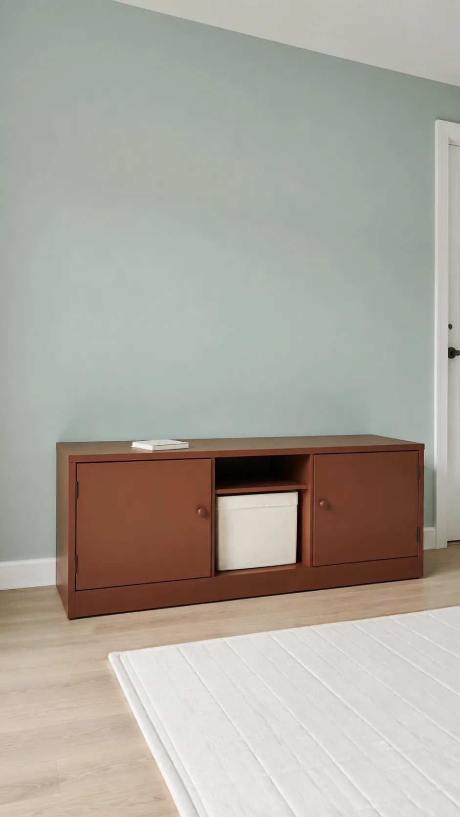 Pale Aqua and Red Clay nursery with red clay low storage cabinet against a broad pale aqua wall