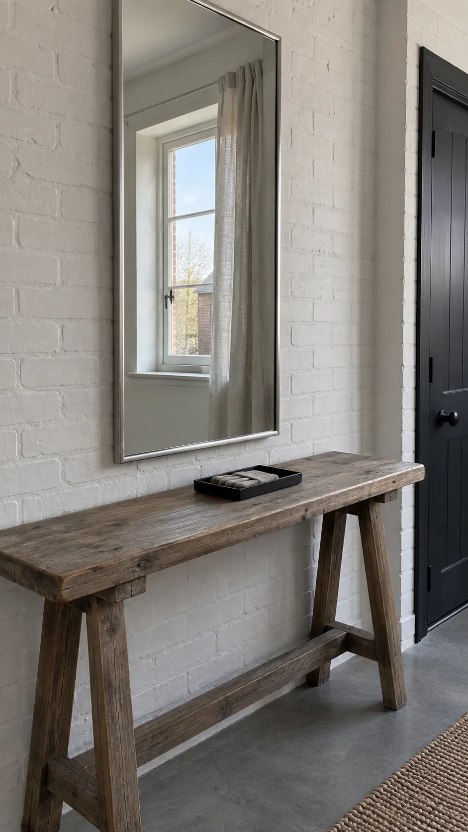 Slim silver mirror reflecting a side window in a brick entryway